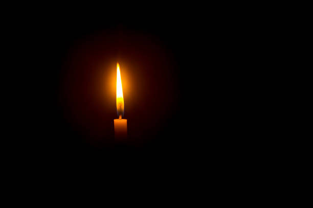 istock A single burning candle flame or light glowing on an orange candle on black or dark background on table in church for Christmas, funeral or memorial service with copy space 1488573649