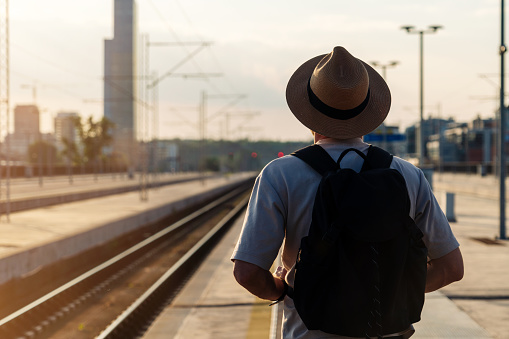Tourist man wearing straw hat standing on the railway platform and waiting train.