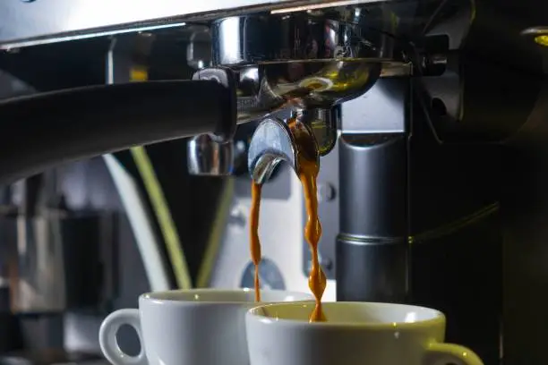 A close-up shot of two cups under a coffee machine pouring coffee