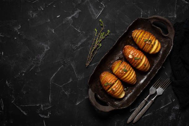 istock Homemade Hasselback Potato with Fresh Herbs thyme. Black stone background. Top view, flat lay, copy space 1488579336