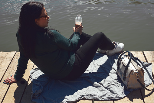 Woman in white sneakers relaxing on a sunny day at the lake wooden deck.