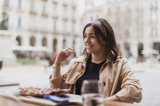 Portrait of happy beautiful young hispanic curvy woman sitting at restaurant. Smiling latin girl eating pizza. Pretty fashionable Spanish lady having dinner at cafe outdoors.