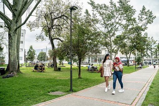 Female student friends are talking while walking through the public park