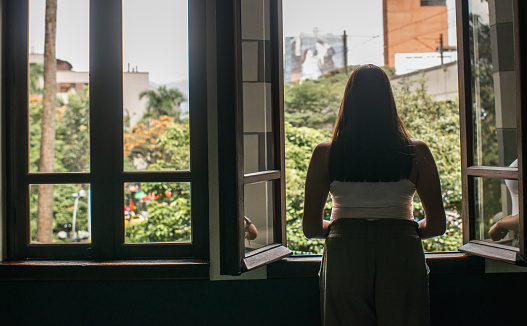 young woman with her back to a window looking outside