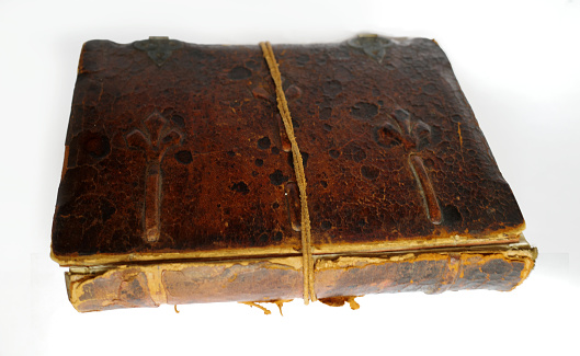 Old weathered book with leather cover and loose spine. It is held together by a leather cord. The background is white
