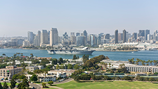 Aerial view of downtown city against military ship during sunny day, San Diego Bay, California, USA.