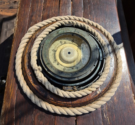 An old ship's compass on a sailboat next to the helm and a nautical rope twisted around.