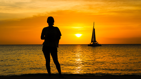 Girl poses in front of sunset over sea with sail boat in background
