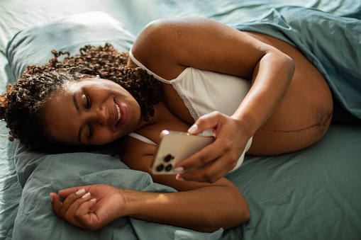 Close up of a Young pregnant woman using a smart phone in the bed in the bedroom