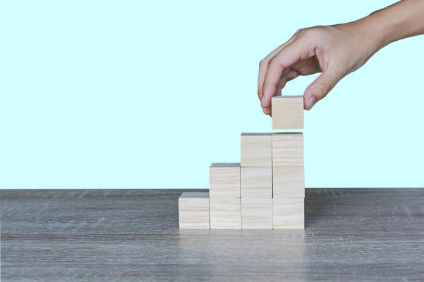 istock Hands stacking wooden blocks as steps on wooden table, light blue background. Business concept for a successful growth process. 1488606095