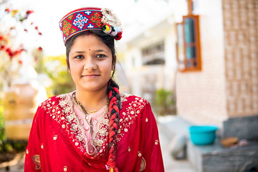 Outdoor portrait of a beautiful traditional young woman of Himachal Pradesh wearing typical Himachali cap and looking at the camera with a smile.