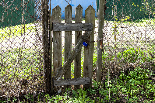 closed old shabby wooden wicket in chain-link fence in backyard in village