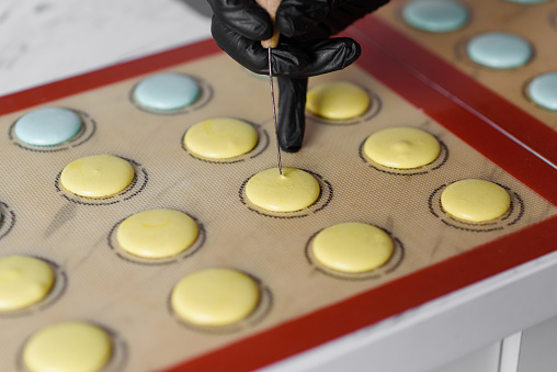 Making macaroons.The process of making macaroni dessert. The pastry chef uses a needle to release air from the dough before baking.High quality photo