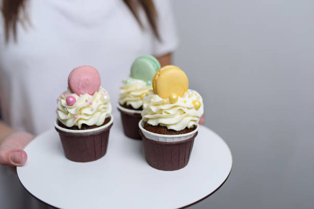 istock A woman holds a tray with three cream-decorated muffins in her hands.Copy space 1488609468