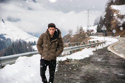 Young man walking on roadside under the snow up in the mountains. Snowy mountain on background