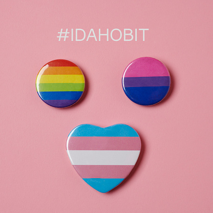 the rainbow, bisexual and transgender flags on a pink background and the hashtag IDAHOBIT, standing for international day against homophobia, biphobia and transphobia