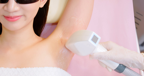 close up overhead view armpit of asian woman lying on bed is receiving underarm hair removal procedure with laser machine and feel relaxed while female doctor holding cosmetology device in clinic