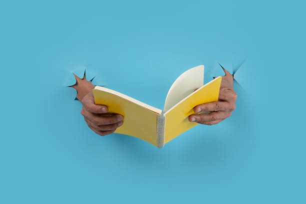 istock Male hand holding a book through blue paper background. 1488613539