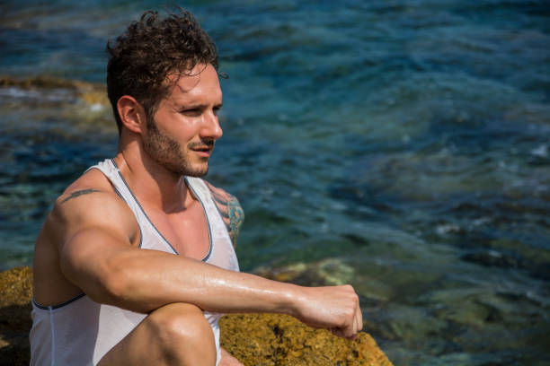 istock Handsome muscular man on the beach sitting on rocks 1488614317