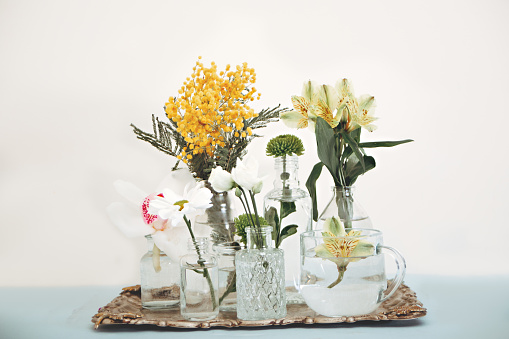 Different vases and glasses on metal tray with beautiful flowers on white background.