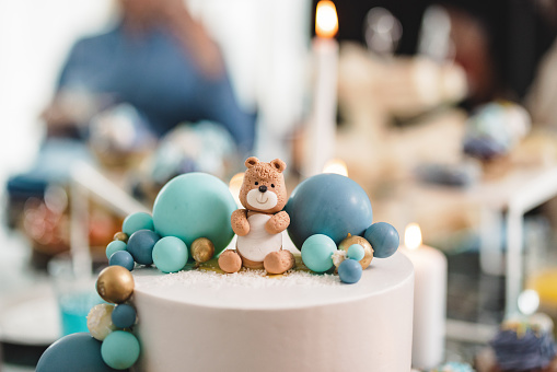 A beautiful white cake with blue decorations and a small teddy bear at a baby shower celebration. A delicious dessert for celebrations and parties.