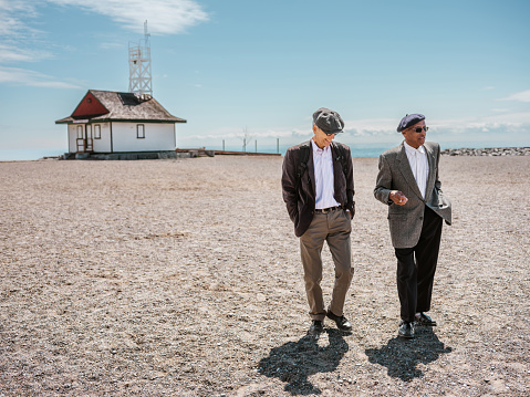 Couple of senior men sightseeing sandy beach at the Lake Ontario. Both dressed in casual classic clothes with sport jacket and hat. Exterior of beach area in Toronto, Ontario.