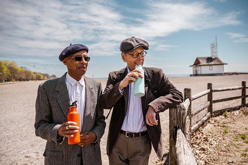 Couple of senior men sightseeing sandy beach at the Lake Ontario. Both dressed in casual classic clothes with sport jacket and hat. Exterior of beach area in Toronto, Ontario.