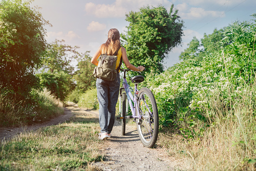 Urban biking woman riding bicycle in city park.Girl on bicycle walks in sunny warm day in the park.Young Woman Riding Bicycle on Free Road in the Forest at Hot Summer Day.Healthy Lifestyle Concept.Girl enjoying bike ride on her way warm summer day.