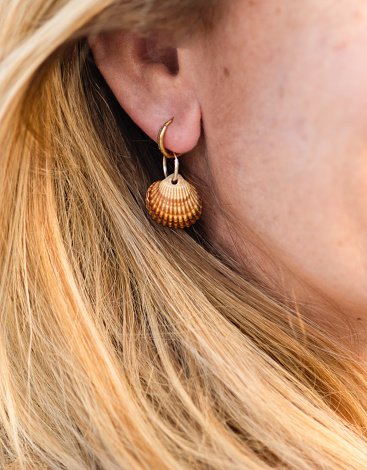 seashell earring detail on the ear of an unrecognizable blonde woman. summer concept and vacations by the beach and the sea. love for the ocean.