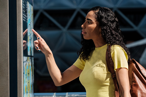 Young woman pointing at display map transport in London. She is wearing a yellow t-shirt and leather backpack. Adventure and transport concept.
