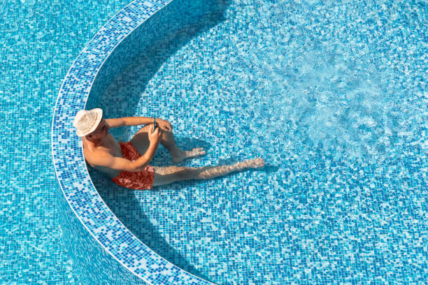 istock Young man relaxing in resort hotel swimming pool, using smartphone, during summer holidays. Tourist vacation, wellness and spa, travel destination. Top view blue water pool background, copy space 1488619642