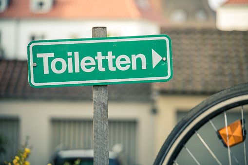 A sign against urban background pointing to the nearest toilet
