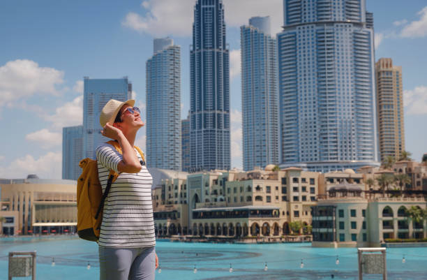 Enjoying travel in United Arabian Emirates. Young woman with yellow backpack walking on Dubai Downtown in sunny summer day.