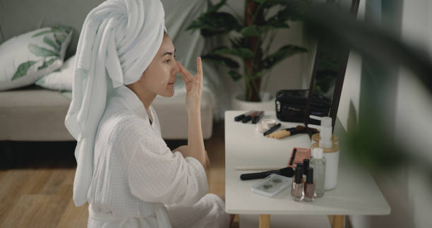 istock Young beautiful woman applying moistuizer on her face at front of mirror 1488620968