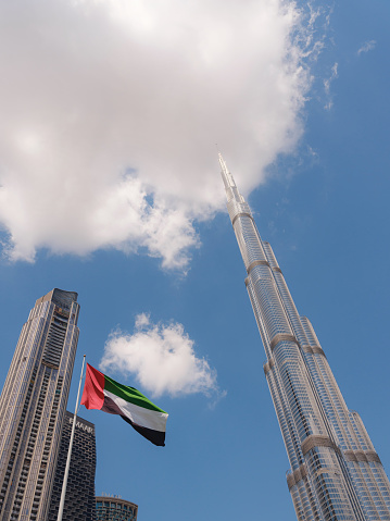 23 March 2023, Dubai, UAE: Burj Khalifa the tallest building in the world with big flag of UAE. Downtown cityscape. Dubai day skyline with clouds, tourist trip to futuristic dubai