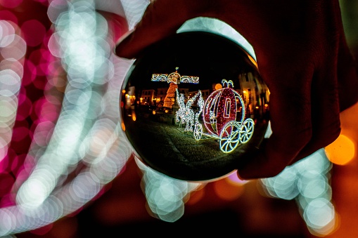 Person holding a ball with reflections of a festive Christmas carriage in the background