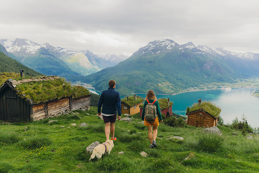 Female and male travellers hiking with a dog in the mountains with view of authentic viking town and the fjord from above in Rakssetra