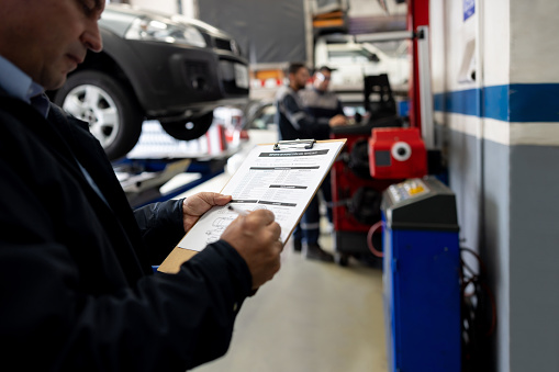 Latin American mechanic working at a car garage and filling a form on a clipboard
