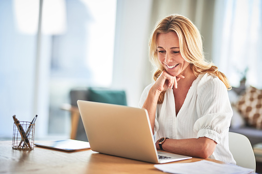 Laptop, remote work and female freelancer working on a creative project in her living room of her house. Happy, confidence and mature woman doing research for business report on computer at her home.