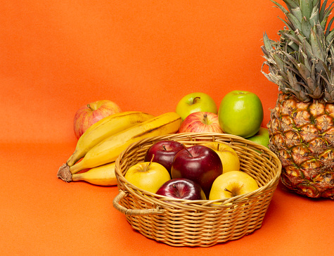 Still life composition of healthy fruits over orange color backgrounds as pineapple, banana and red, yellow and green color apples fruits. Image made in studio of healthy eating concept.
