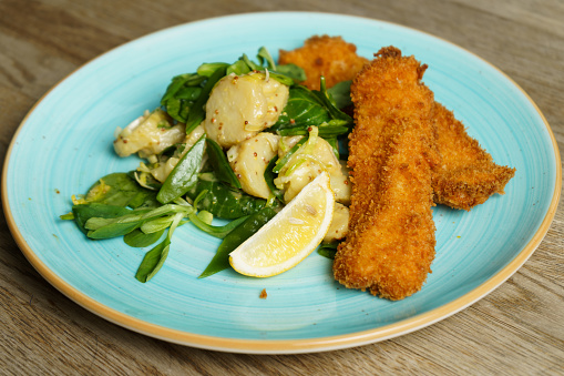 Fried cod fish fillet with potato salad, dijon mustard and a slice of lemon on a plate