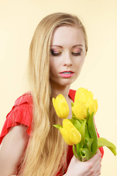 Beautiful young blonde woman holding tender white flower near face, skincare concept