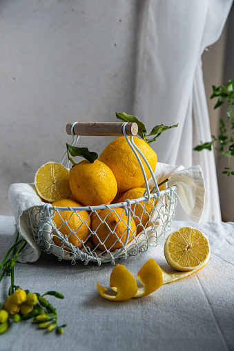 Fresh Italian lemons with leaves in white wire basket on linen tablecloth.