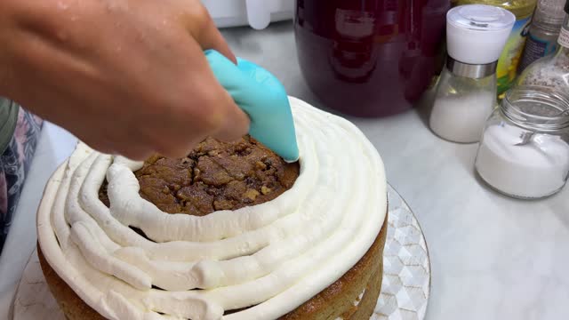 Chef applies white cream with a pastry bag in a circle on a brown cake