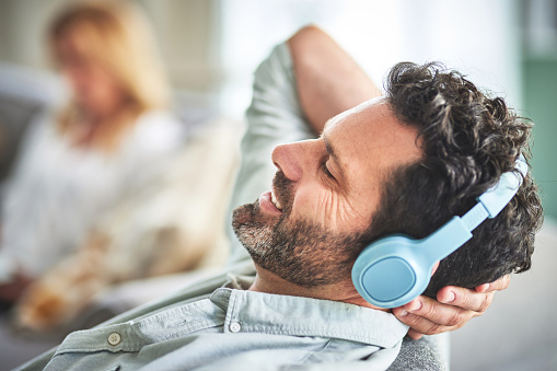 Relax, music and smile with man in living room for streaming, mobile radio and podcast. Technology, audio and headphones with male listening to sound at home for peace, weekend break and calm