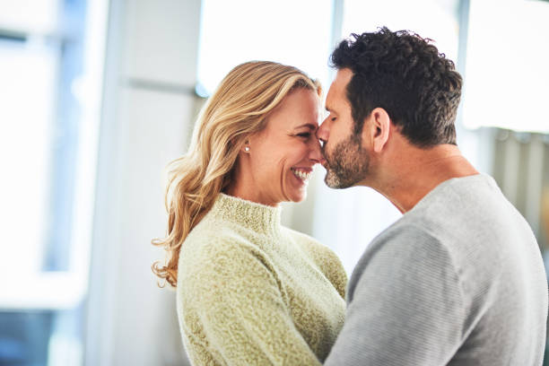 Love, happiness and couple kiss in home, romance and bonding together in house with smile on face. Marriage, happy woman and mature man hug in apartment, romantic quality time and hugging in morning. stock photo