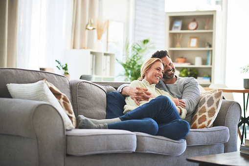 Couple hug on sofa, watching tv and relax together at home, love and trust with connection and spending time together. Happy people in living room, bonding and online streaming service subscription