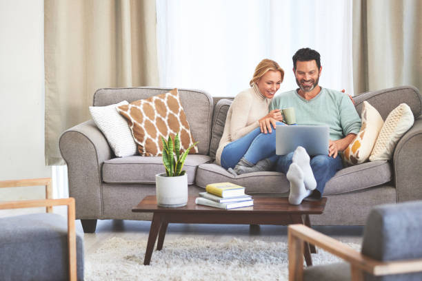 café, pareja y feliz con computadora portátil en la sala de estar de casa, unión y relajación. té, sofá y hombre y mujer con computadora, viendo y transmitiendo video, película o película juntos en el sofá de la casa. - couple home interior laptop computer fotografías e imágenes de stock