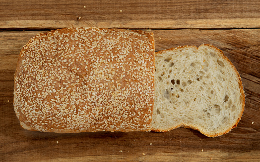 Top view of a loaf of bread made from sourdough, slice of fresh bread on a wooden table. Sesame seeds on homemade bread. bakery. traditional. rustic. natural.