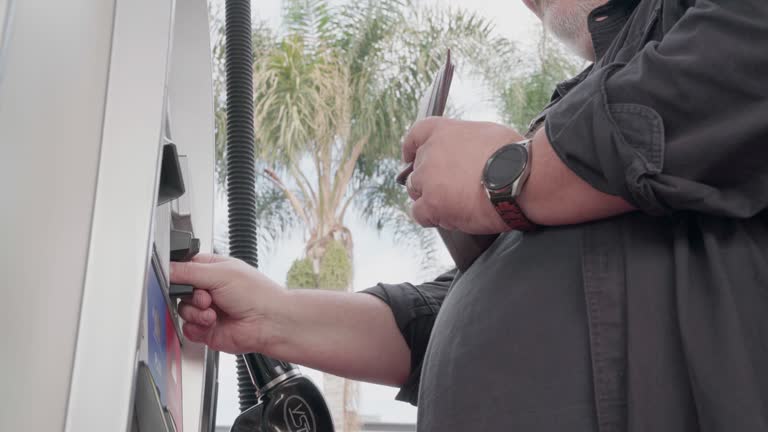 Mature Caucasian Man Using a Credit Card to Buy Fuel at a Self-Service Gas Pump on an Overcast Day in California, USA